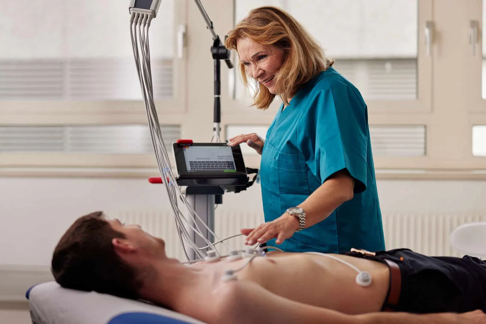 Ärztin legt einem liegenden Patienten ein EKG an